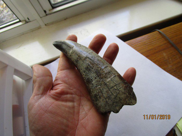 A hand holding an old metal object in front of a window.